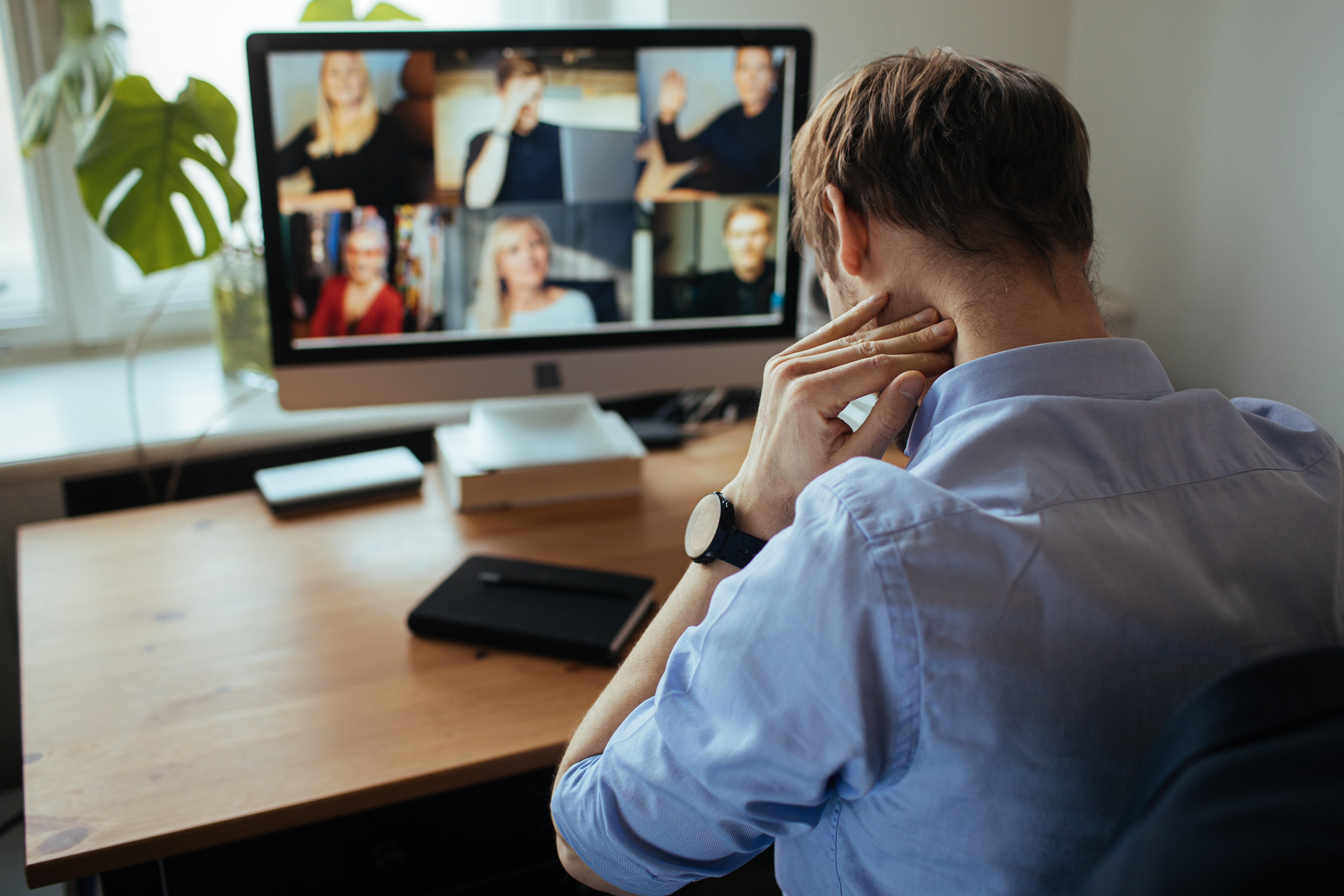 Ein Mann sitzt vor einem Bildschirm und folgt einer Videonkonferenz.