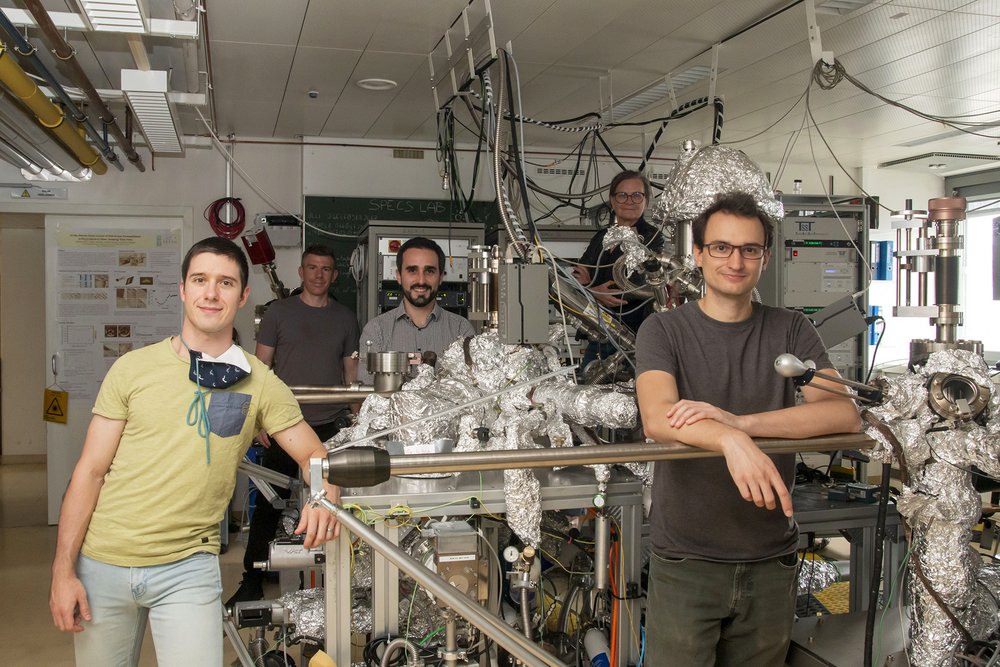 Das fünfköpfige Team in einem großen Forschungslabor, rings um eine große Vakuumanlage.