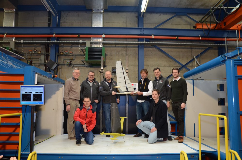 A group of people is standing in a wind tunnel. One person is holding a model sailboat in his hand. 