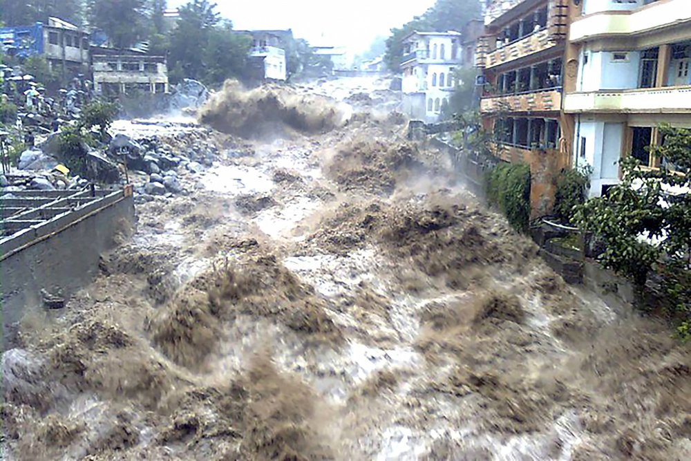 A muddy river carries brown water and destroys the adjacent houses.