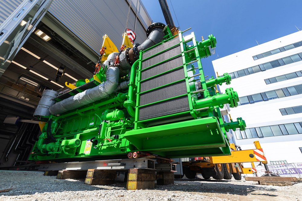 A large green engine is lifted into a hall.