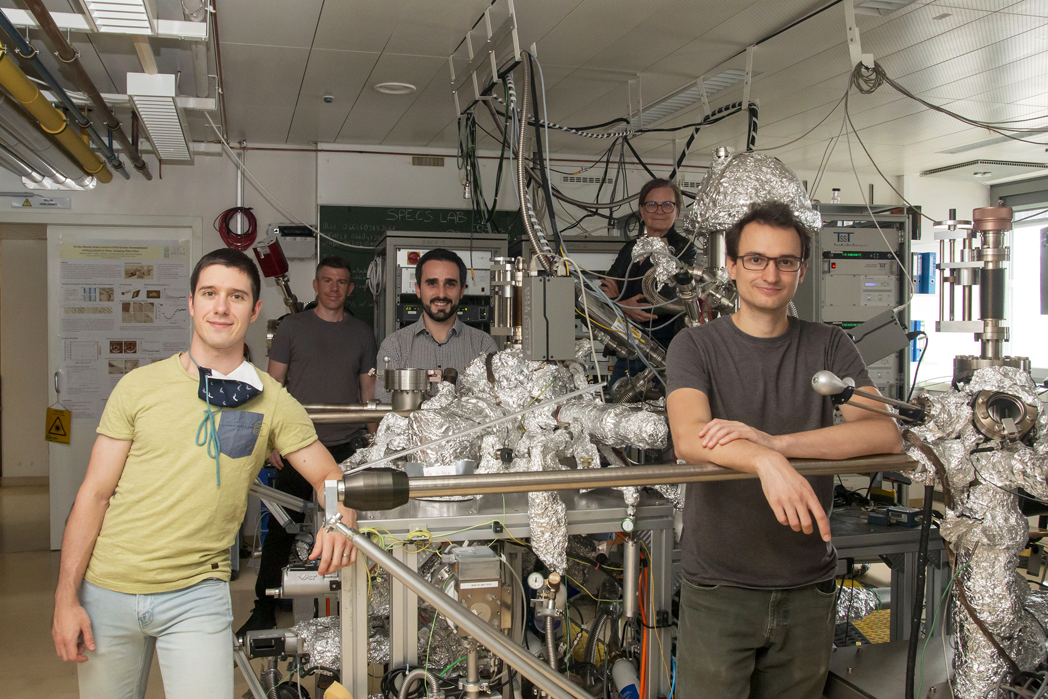 The 5-person team in a large research laboratory, all around a large vacuum system.
