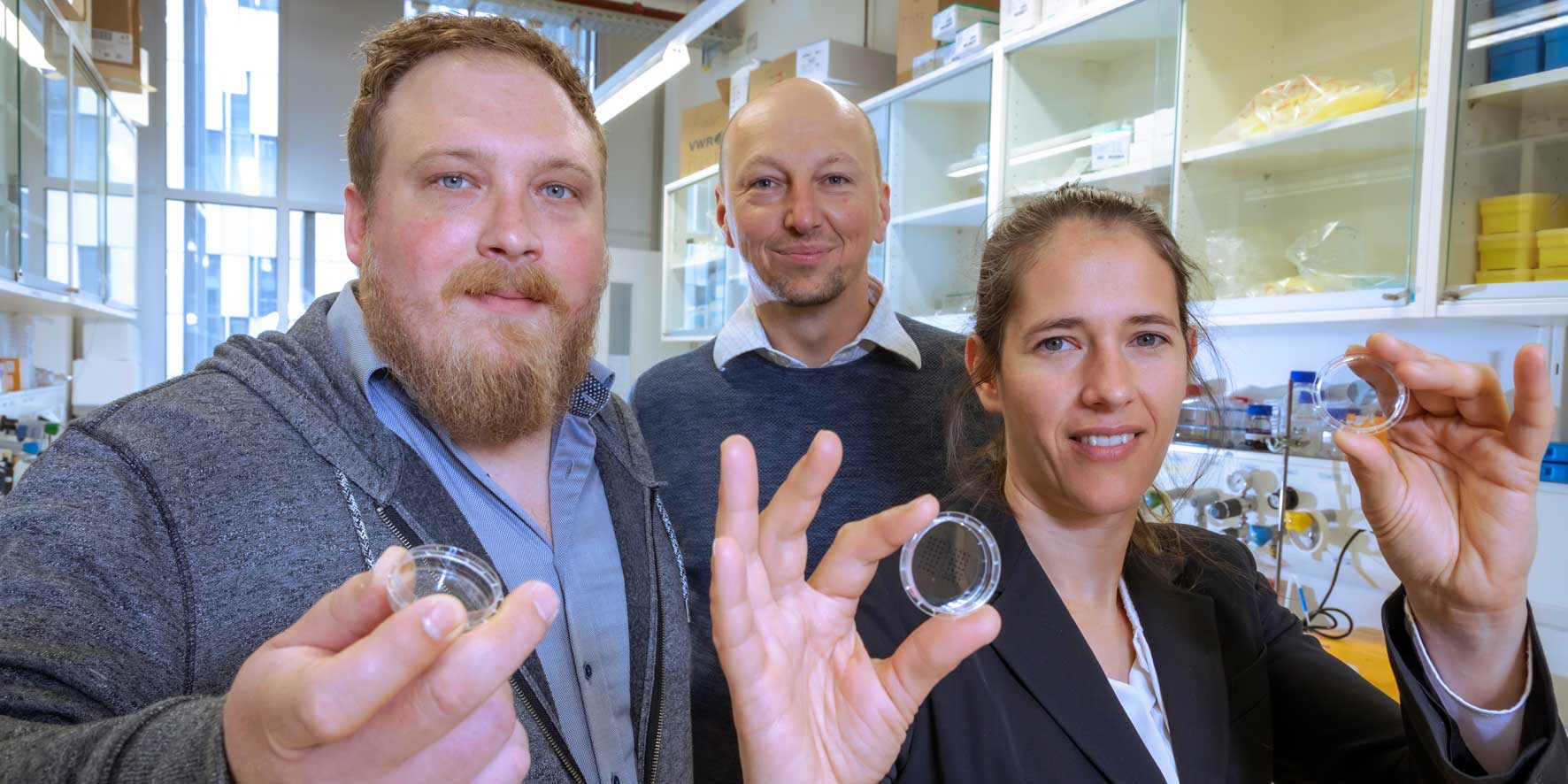 Two researchers from Med Uni Graz and a female researcher from TU Graz hold Petri dishes up to the camera