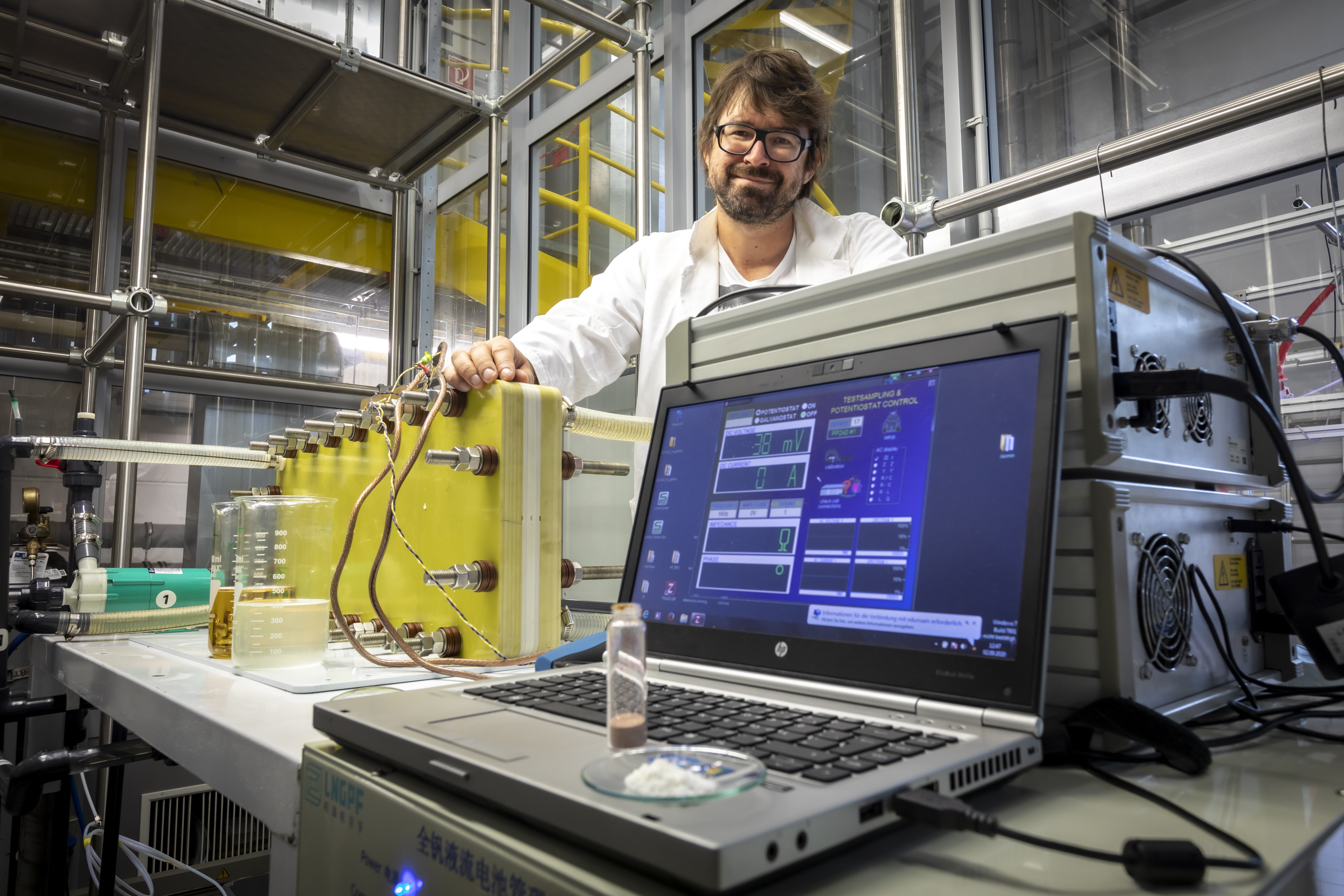 Ein Mann steht in einem Labor hinter einem Stromspeicher und einem Laptop.