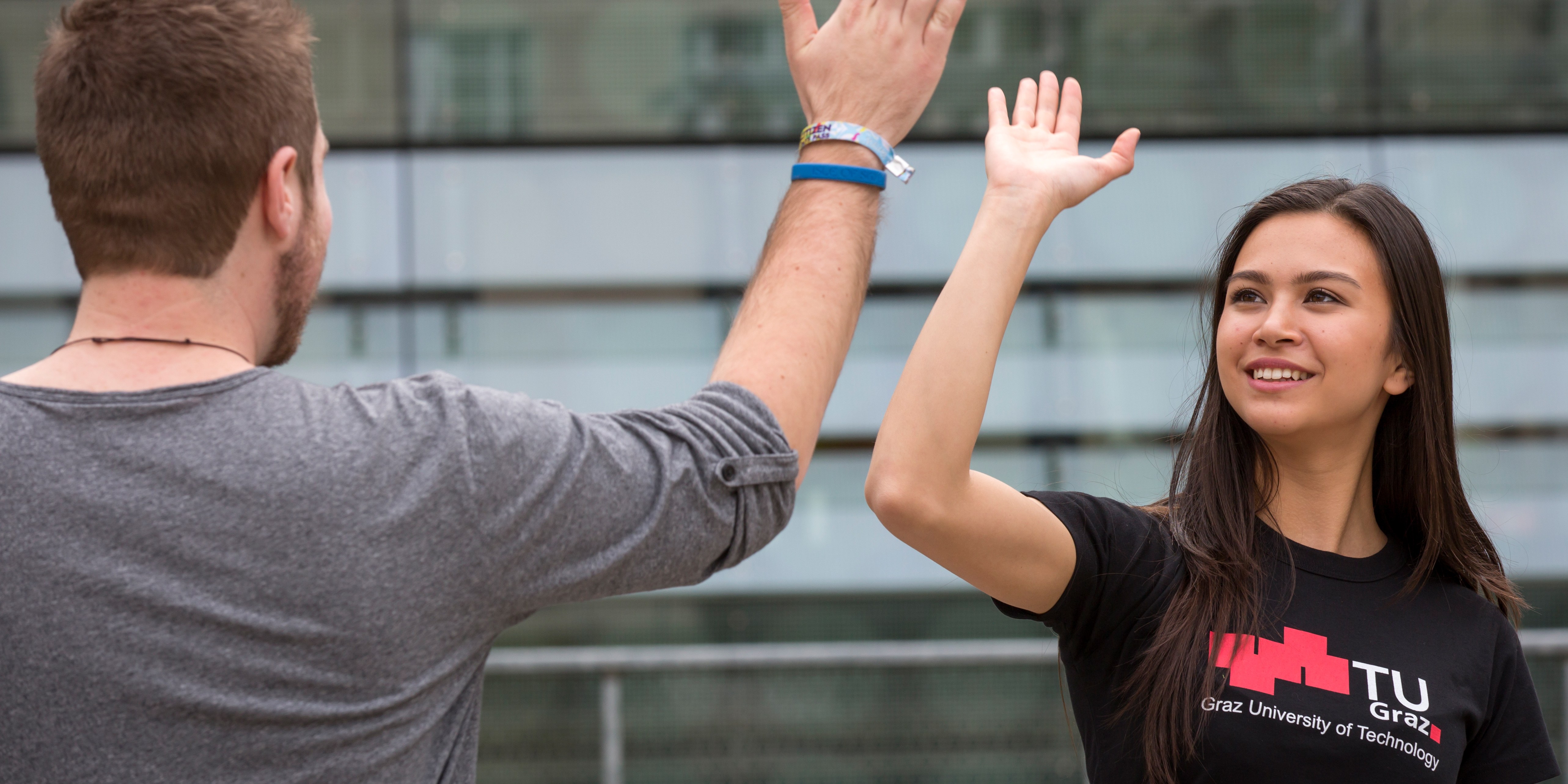 A male student wearing a grey shirt and a female student wearing a black TU Graz shirt give each other a high five.