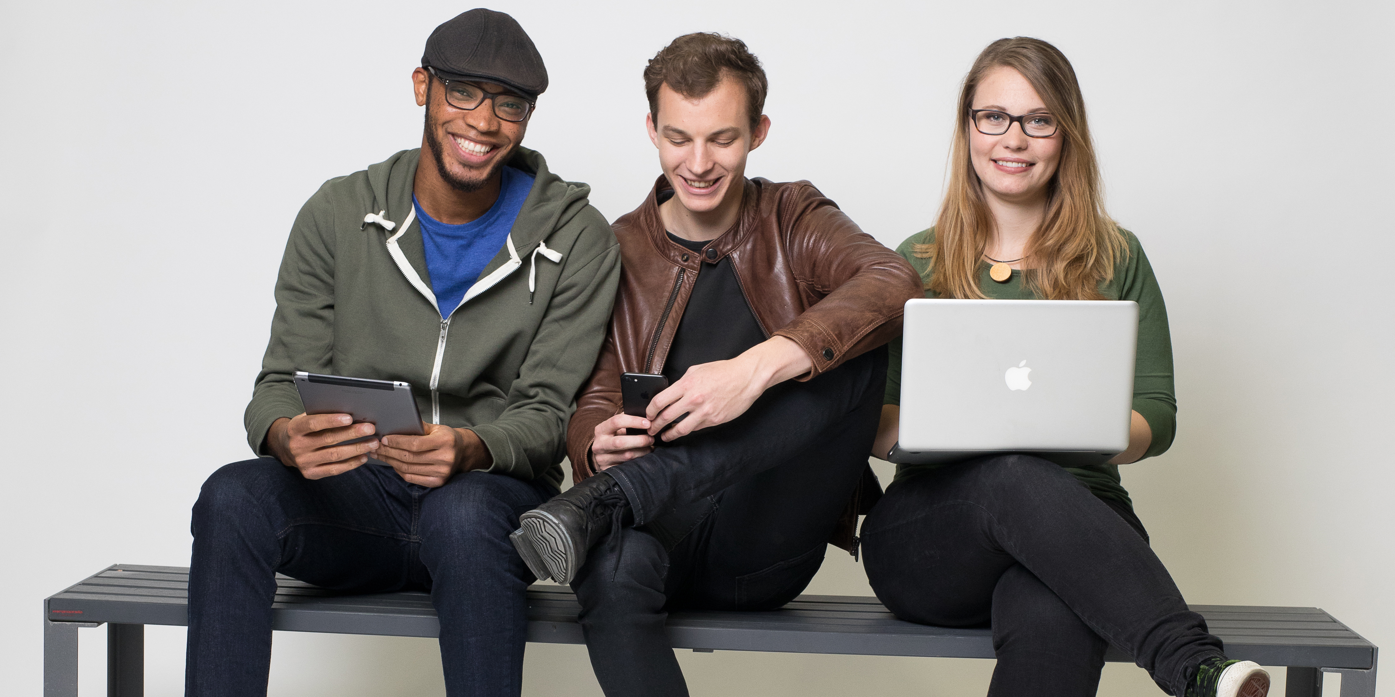 Zwei Studenten und eine Studentin der TU Graz auf einer grauen Bank mit Laptop und Tablet.